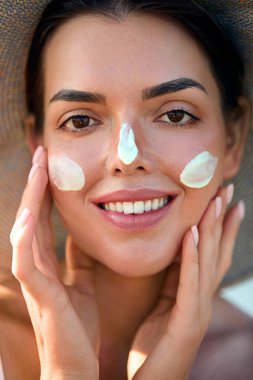 Yüz kremi sürerken gülümseyen güzel bir kadın, cilt bakımını ve sağlıklı cilt bakımını güzellik ve sağIık için uyguladığını vurgulayarak. Deri Bakımı Konsepti.
