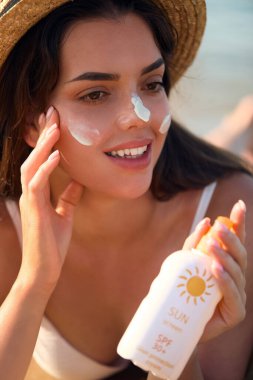 Cilt Bakımı Konsepti. Güneş koruması. Şapkalı Güzel Kadın yüzüne güneş kremi sür. Plajda güneş kremi sürmüş bir kadın. Kadın Tutucu Nemlendirici Güneş kreminin Portresi. Bir Kız Cilt İçin Güneş kremi Kullanıyor. 