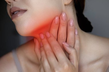 Bir kadın boynuna acı dolu bir ifadeyle dokunuyor. Rahatsızlık ya da gerginlik belirtisi. Boğazı ağrıyan, öksüren, soğuk bir kadın portresi.