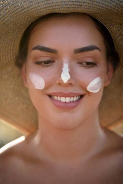 Yüzüne güneş kremi süren güzel bir kadın gülümsemesi. Deri ve Vücut Bakımı. Güneş koruması. - Evet. Şapka lekeli kadın nemlendirici losyon ya da cilt üzerinde güneş kremi
