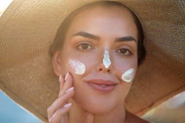 Cilde nemlendirici losyon süren bir kadının portresi. Yüzünde güneş kremi olan güzel bir kadın. Cilt bakımı kavramı. Güneş koruması. Güneş yanığı