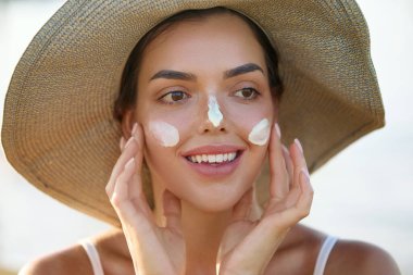 Genç ve güzel bir kadın güneş kremi sürüyor ve kendi yüzüne dokunuyor. Cilt bakımı. Güzellik Konsepti. Cilde kadın güneş kremi sürmüş. Cilt Koruma ve Dermatoloji.