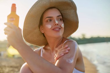 Kadın plajda bronzlaşmadan önce omzuna güneş kremi sürüyor. Güneş kremi. Güneş yanığı. Güneş kremi süren güzel bir kadın. Cilt bakımı. Güneş koruma kavramı.