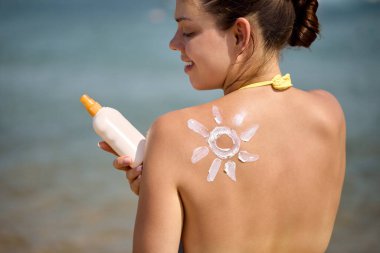 Güneş kremi. Güneş kremi, bronzlaşmış omuzlara güneş şeklinde süren güzel bir kadın. Güneş kremi mi. Cilt bakımı. Güneş koruması. Kız Nemlendirici Güneş kremi Kullanıyor