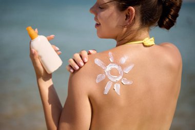 Güneş kremi, bronzlaşmış omuz ve güneş şeklinde. Güneş koruması. Güneş kremi süren bikinili güzel bir kadın. Cilt ve vücut bakımı. Güneş kremi ya da nemlendirici güneş kremi tutan kadın portresi..