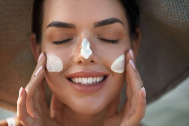 Yüzüne güneş kremi süren güzel bir kadın gülümsemesi. Deri ve Vücut Bakımı. Güneş koruması. - Evet. Şapka lekeli kadın nemlendirici losyon ya da cilt üzerinde güneş kremi