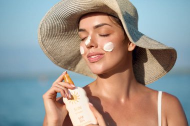 Güzel kadın tabaklanmış bir yüze krem güneş kremi uyguluyor. Güneş. Cilt ve vücut bakımı. Kız cildi için güneş kremi kullanıyor. Güneş losyonu tutan ve nemlendirici güneş kremi tutan bir kadın portresi.