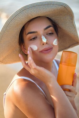 Kadın uygulanan güneş kremi yüzündeki gülümseme. Cilt Bakımı. Vücut güneş koruması. Güneş kremi. Kadın şapka smear losyon cildinize nemlendirici