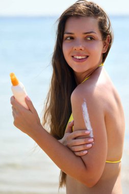 Güneşli bir plajda güneş kremi süren güzel bir kadının portresi cildini zararlı ultraviyole ışınlardan korurken dışarıda geçirdiği günün tadını çıkarıyor. Cilt bakımı kavramı.
