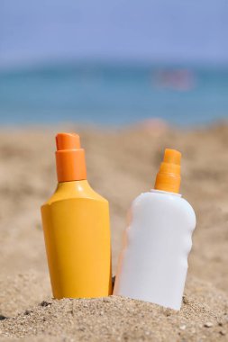 Deniz ve mavi gökyüzü zeminli kumlu plaja iki güneş kremi şişesi yerleştirildi. Yazı, güneşi ve tatilleri tasvir etmek için mükemmel..
