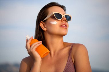 Güneş Kremini Tenine Kullanan Bir Güzel Kadın. Bronzlaşmış Yüze Güneş kremi süren Güzel Kadın. Güneş kremi tutan kadın portresi ya da nemlendirici güneş kremi. Güneş koruması. Cilt ve Vücut Bakımı.