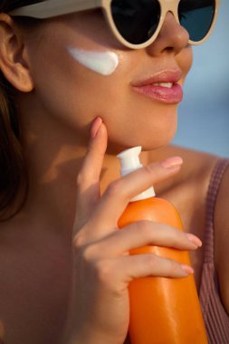 Güneş kremi süren güneş kremi kullanan kadın. Güzel, mutlu, tatlı bir kız cildine krem sürüyor. Elinde losyon ya da nemlendirici güneş kremi tutan bir kadının portresi.