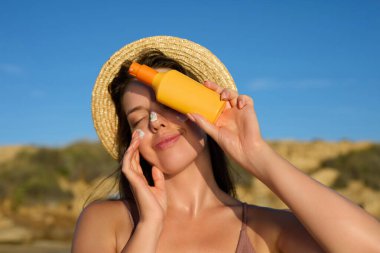 Bikini 'deki Güzel Kadın Bronzlaşmış Yüze Güneş kremi sürüyor. Güneş koruması. Güneş kremi kullanan kız derisi. Güneş kremi tutan kadın portresi ya da nemlendirici güneş kremi. Cilt ve Vücut Bakımı.