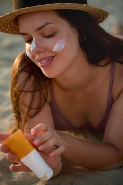 Bikini 'deki Güzel Kadın Bronzlaşmış Yüze Güneş kremi sürüyor. Güneş koruması. Güneş kremi kullanan kız derisi. Güneş kremi tutan kadın portresi ya da nemlendirici güneş kremi. Cilt ve Vücut Bakımı.