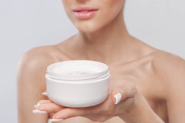 Cilt bakımı. Güzellik Konsepti. Kozmetik nemlendirici krem tutan genç bir kadın. Yumuşak cilt, çıplak omuzlar, açık makyajlı manken, temiz ciltli kız yüzü portresi. Dermatoloji