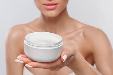A woman presents a jar of cream with a smooth texture, highlighting her radiant skin. The soft background emphasizes her natural beauty and skincare routine.