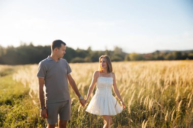 Güneş batarken el ele tutuşarak, sıcak yaz akşamı havasında romantik bir atmosfer yaratarak, altın bir tarlada birkaç tur atar..