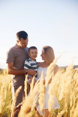 Ebeveynler gün batımında küçük oğullarını altın bir tarlada tutarlar, güneş onların gülümsemelerini aydınlatırken çimenler rüzgarda sallanırken..