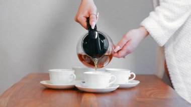 Beyaz çay fincanlarına çay dolduran kadın. Bir kadın eli, dört beyaz çay fincanına cam bir çaydanlıktan çay dolduruyor.