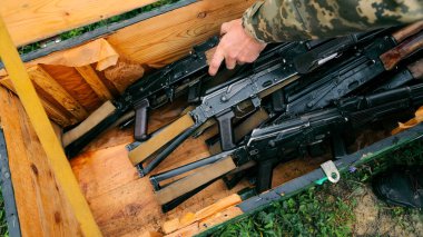 Close-up of automatic rifles in a wooden crate. A close-up view of several automatic rifles neatly arranged in a wooden crate, with a persons hand reaching in clipart