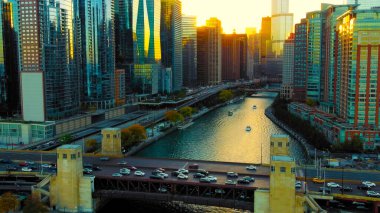 Chicago Illinois 17.10.2024. Gün batımında gökdelenleri olan Chicago nehri manzarası. Şikago nehrinin ve gün batımında gökdelenlerin sıcak altın ışıklarını yansıttığı ikonik bir ufuk çizgisi.