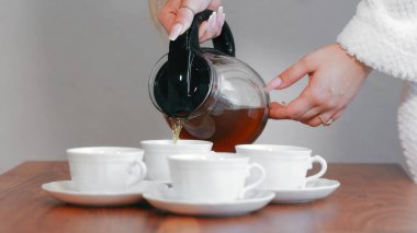 Beyaz bardaklara çay dolduruyorum. Bir insanın elleri dikkatle çaydanlıktan çaydanlığı ahşap bir masaya yerleştirilmiş dört beyaz fincana döküyor.