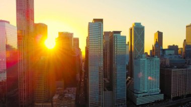 Gün batımında altın güneş ışığıyla gökdelenler. Canlı bir şehir silueti, güneş batarken altın güneş ışığıyla yıkanır. Yükselen gökdelenleri aydınlatır ve uzun gölgeler oluşturur.