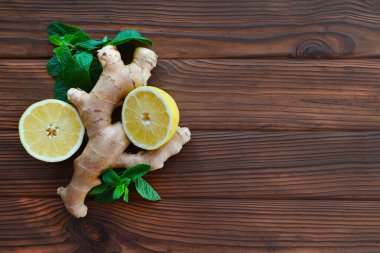 Zencefil kökü, limon dilimleri ve ahşap yüzeyde nane yaprakları. Taze zencefil kökü, iki limon dilimi ve kırsal ahşap bir yüzeye yerleştirilmiş canlı nane yaprakları. Üst Manzara. Boşluğu kopyala