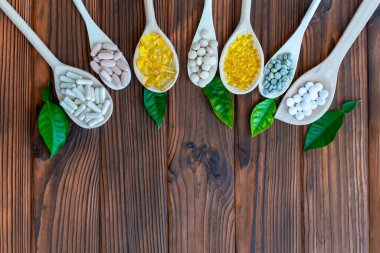 Variety of supplements on wooden spoons with green leaves. Wooden spoons are arranged in a row, each filled with different types of supplements. Top view. Free space for text clipart