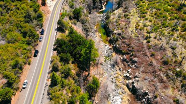 Engebeli kanyon manzarasının yanındaki yol manzarası. Bir hava manzarası kayalık bir kanyonun yanında, ender yeşillik ve akan bir akarsu ile dolambaçlı bir yol yakalar.