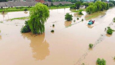 Kamyon Yüksekte Gezinirken Kırsal Arazi 'yi sel basmış. Su altında kalmış ağaçlar ve binalarla çevrili bir kamyonun yüksek sularda yüzdüğü taşra bölgesinin hava görüntüsü.