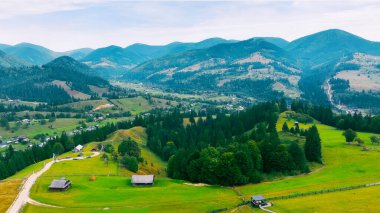 Yeşil vadileri olan manzaralı dağ köyü. Bereketli yeşil tarlalar, yuvarlanan tepeler ve sık ormanlarla çevrili pitoresk bir dağ köyünün havadan görünüşü huzur verici bir manzara yaratıyor.