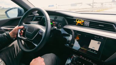 Drivers hands on steering wheel in modern car. Close-up of a drivers hands on the steering wheel of a modern car, with visible digital dashboard and infotainment system displaying navigation and radio clipart