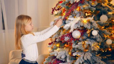 Noel Ağacı 'nı süsleyen kız. Genç bir kız Noel ağacını süs ve ışıklarla süsleyerek evde sıcak ve rahat bir tatil ortamı yaratıyor.