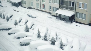 Kış fırtınasında karla kaplı park edilmiş arabalar. Kış fırtınası sırasında park halindeki araçlar yoğun bir şekilde bir yerleşim yerinin önünde karla örtülüdür.