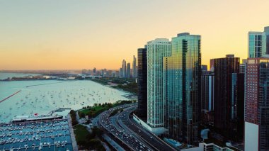 Chicago Skyline ve Marina Sunset 'te. Şikago 'nun hava manzarası sakin bir günbatımında tekne, otoyol ve Michigan Gölü ile dolu marinayla birlikte yükseliyor.