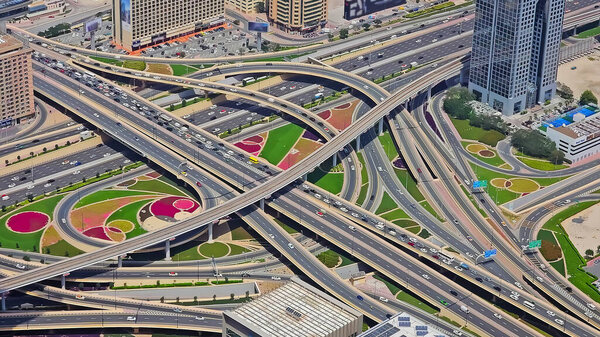 Вид с воздуха на сложную городскую развязку. Снимок с воздуха, показывающий разрастающуюся многоуровневую дорожную развязку в городе, с многочисленными полосами движения, путепроводами и ландшафтными зонами