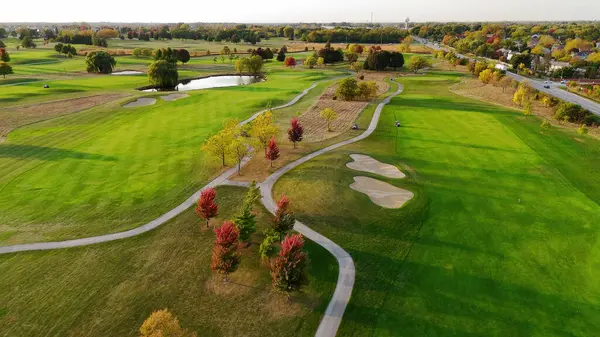 Sonbaharda golf sahasının havadan görünüşü. Kum sığınakları, patikalar, göletler ve yeşillikleri kaplayan renkli sonbahar ağaçları olan yemyeşil bir golf sahasının manzaralı bir görüntüsü.