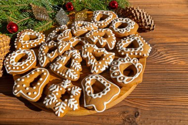 Assortment of holiday gingerbread cookies with decorative details. A collection of holiday-themed gingerbread cookies with intricate white icing designs in various shapes arranged on a wooden plate clipart