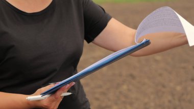 Kağıtları dışarıda tutan kişi panosu. Siyah tişörtlü birinin elinde belgelerle açık bir alanda duran ve dışarıda çalışan bir pano tutarken yakın plan fotoğrafı.