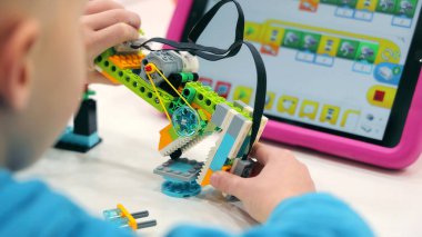 Tabletle Çocuk Robot Geliştirme Projesi. Renkli bir robot kitini programlama talimatlarını gösteren bir tabletle birleştiren küçük bir çocuk