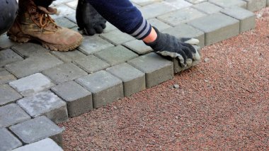 Çakıl üzerinde beton kaldırımlar döşeyen işçi. Sıkıştırılmış çakıl üzerinde beton kaldırımları hizalayan bir işçinin yakın çekimi