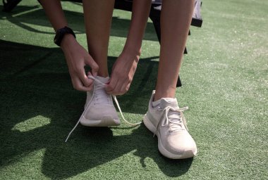 Koşu ayakkabılarına bağlama sporcusu. Yeşil bir çim yüzeyinde otururken açık renkli bir koşu ayakkabısının bağcıklarını bağlayan bir sporcunun yakın plan fotoğrafı.