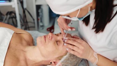 Spa Kliniğinde Kozmetik Prosedür. Klinik kaplıca ortamında bir kadının alnına kozmetik enjeksiyon yapan bir profesyonelin yakın plan çekimi.