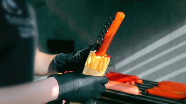 Preparing hot dog with ketchup and bun. Close-up of hands in black gloves inserting a hot dog sausage into a bun with ketchup, in a professional grilling setup clipart