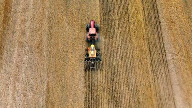 Tractor plowing a field from above. Aerial view of a red tractor working in a dry field, showcasing the agricultural process of plowing and preparing the soil for planting clipart