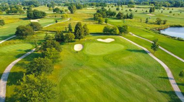 Yeşillikle birlikte golf sahasının havadan görüntüsü. Yeşillik çayırların, kum depolarının, ağaçların ve doğal güzelliklerle çevrili patikaların bulunduğu manzaralı bir golf sahası manzarası.