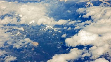 Bulutların ve Dağ manzarasının hava görüntüsü. Karlı zirveleri ve engebeli arazisi olan bir sıradağda nefes kesici hava manzarası kabarık bulutlar sergiliyor.