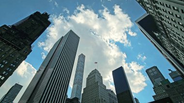 Skyscrapers and Cloudy Blue Sky Perspective. Low-angle view of modern skyscrapers against a vibrant blue sky with scattered clouds clipart