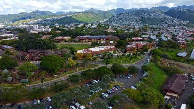 Honolulu, Hawaii 'deki Lush Kampüsü' nün hava görüntüsü. Honolulu, Hawaii 'de, tropik ağaçlar, modern binalar ve manzaralı dağ manzaralarıyla çevrili yeşil bir kampüsün hava görüntüsü.